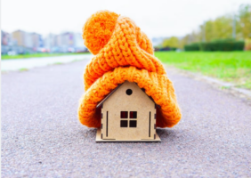 Little wodden house on the road with a large orange wooly hat