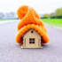 Little wodden house on the road with a large orange wooly hat