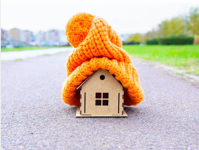 Little wodden house on the road with a large orange wooly hat