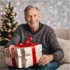 Elderly man sitting besdie the Christmas tree and holding a Christmas present