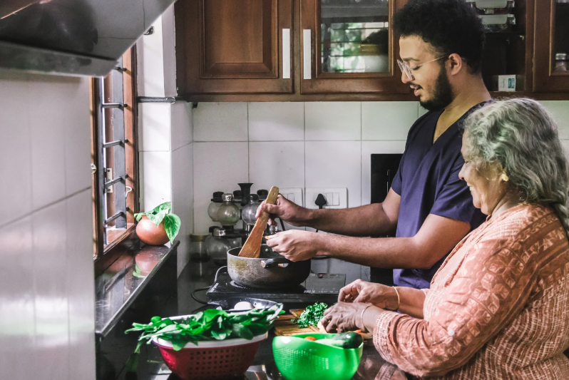 Adult son helping his elderly mother prepare dinner in the kitchen